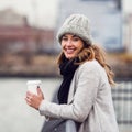 smiling woman drinking coffee from paper cup standing on river embankment and enjoying the view