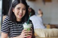 Smiling woman drinking matcha green tea latte in the morning at coffee shop. Portrait pretty Asian girl holding green tea glass in Royalty Free Stock Photo