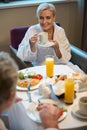 Smiling woman drinking tea or coffee and looking at partial man having breakfast Royalty Free Stock Photo