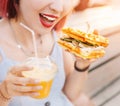 Smiling woman drinks fresh juice and eats a delicious sandwich with a loaf of a checkered Viennese waffle Royalty Free Stock Photo