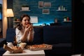 Smiling woman eating a slice of hot pizza delivery sitting on couch looking at family show on television Royalty Free Stock Photo