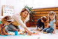 Smiling woman educator playing with children sitting on floor in kindergarten. Kids folding lego and drawing with Royalty Free Stock Photo