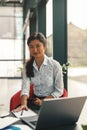 Smiling woman entrepreneur holding phone and looking at camera while working on laptop in office Royalty Free Stock Photo