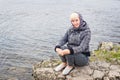 Smiling woman fifty years in a scarf on his head sitting on a stone near the river