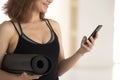 Smiling woman fitness instructor holding yoga mat, using phone