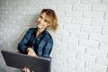 Smiling woman freelancer with laptop in her hands standing against white brick wall