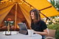 Smiling Woman freelancer using a laptop on a cozy glamping tent in a sunny day. Luxury camping tent for outdoor summer holiday and Royalty Free Stock Photo