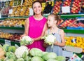 Woman with girl holding cabbage in vegetables section Royalty Free Stock Photo