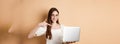 Smiling woman in glasses pointing finger at laptop screen, showing online promo, standing on beige background Royalty Free Stock Photo