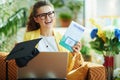 Smiling woman with graduation cap and laptop showing textbook