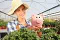 Smiling woman in greenhouse, with piggy bank,