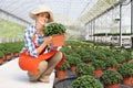 Smiling woman in greenhouse, with a potted plant