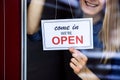 Smiling woman hanging open sign on small local business shop door window