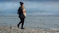 Smiling woman in hat and scarf walking on ocean beach and collecting beautiful sea shells. Concept of hiking, travel, exploration Royalty Free Stock Photo