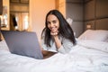 Smiling woman with her legs raised slightly in front of her laptop lying on the bed Royalty Free Stock Photo