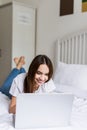 Smiling woman with her legs raised slightly in front of her laptop lying on the bed. Royalty Free Stock Photo