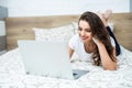 Smiling woman with her legs raised slightly in front of her laptop lying on the bed. Royalty Free Stock Photo