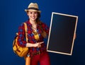 Smiling woman hiker isolated on blue pointing at blank board