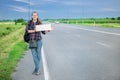 Smiling woman hitchhiker on the road is holding a blank board