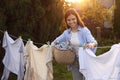 Smiling woman holding basket and hanging clothes with clothespins on washing line for drying in backyard Royalty Free Stock Photo