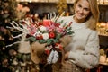 Smiling woman holding a christmas composition with pink orchids, white roses, fir-tree branches, red apple and candle in Royalty Free Stock Photo