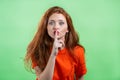 Smiling woman holding finger on her lips over green background. Gesture of shhh, secret, silence. Close up. Royalty Free Stock Photo