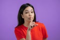 Smiling woman holding finger on her lips over violet background. Gesture of shhh, secret, silence. Close up.