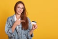 Smiling woman holding gold credit card and pointing on it with her index finger, copy space for advertismant or promotin text, Royalty Free Stock Photo