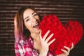 Smiling woman holding heart shape against brick wall Royalty Free Stock Photo
