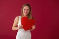 Smiling woman holding papper heart in hands on red background