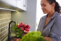 Smiling woman holding radish, standing by kitchen counter with a cardboard box full of delivered fruits and vegetables Royalty Free Stock Photo