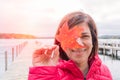 Smiling woman holding a red maple leaf in front of her face