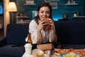 Smiling woman holding tasty burger in hands looking at television comedy sitcom standing on couch Royalty Free Stock Photo