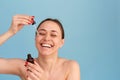 Smiling woman holding vitamin c serum near her face on blue background. Skin care and health concept