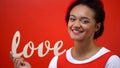 Smiling woman holding wooden love sign closeup, Saint Valentines Day celebration