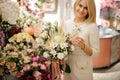 Smiling woman holds exclusive bouquet of different white flowers decorated with greenery in her hand