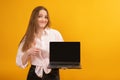 Smiling woman holds laptop with blank screen and showing thumbs up. Copy space, mock up. Studio portrait isolated on yellow Royalty Free Stock Photo