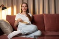 Smiling woman at home sitting on the couch and watching tv, she is holding a remote control and eating popcorn Royalty Free Stock Photo