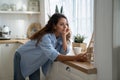 Smiling woman housewife standing in kitchen reading latest news on phone, ordering groceries online