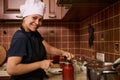 Smiling woman housewife in white chef hat and apron, using seamer, closes lids of jars with freshly canned tomato sauce Royalty Free Stock Photo