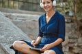 Smiling woman listen music in headset with modern tablet. Relax and joy in park. Leisure time and take break concept