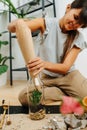 Smiling woman in living room planting inside glass bottle, using paper cone