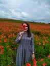 Smiling woman in a long gray dress standing on the red poppy field Royalty Free Stock Photo