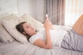 Smiling woman looking at mobile phone lying down on white bed. H Royalty Free Stock Photo