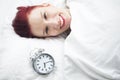 Smiling woman lying in bed with alarm clock on pillow Royalty Free Stock Photo