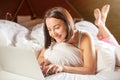 A smiling woman lying down the bed in front of her laptop with her legs raised slightly Royalty Free Stock Photo