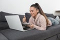 smiling woman lying on sofa with thumbs up taking notes on laptop computer Royalty Free Stock Photo