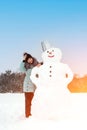 smiling woman makes a snowman on a winter day in a snow-covered field under the open sky. Royalty Free Stock Photo