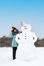 smiling woman makes a snowman on a winter day in a snow-covered field Royalty Free Stock Photo