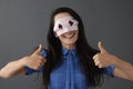 Smiling woman in mask on face holds thumbs up